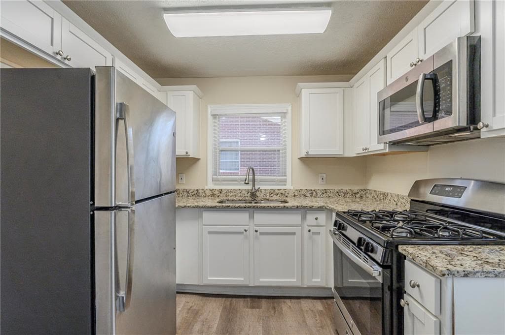 Kitchen with white cabinets, stone counters, a gas range, a microwave and a refrigerator