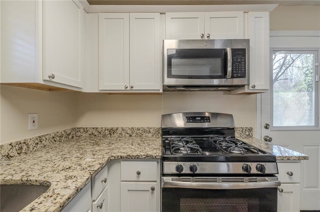 Gas range and microwave between white cabinets and stone counters